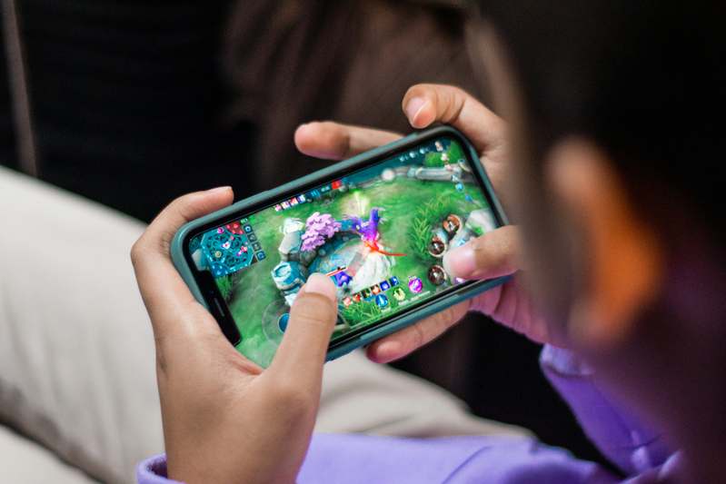 Person playing a casual mobile game on a tablet while lounging on a couch with soft natural light